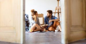 Two first time buyers sitting on the floor in their new house with moving boxes behind them