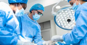 Three doctors wearing blue scrubs performing surgery