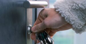 Someone wearing a grey wool jumper using a pair of keys to unlock the front door