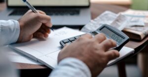 A man using a calculator while writing notes in his note pad