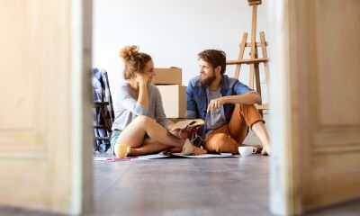 Two first time buyers sitting on the floor in their new house with moving boxes behind them