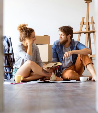 Two first time buyers sitting on the floor in their new house with moving boxes behind them