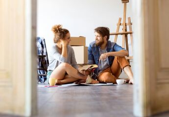 Two first time buyers sitting on the floor in their new house with moving boxes behind them