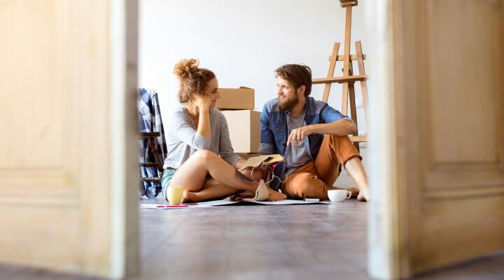 Two first time buyers sitting on the floor in their new house with moving boxes behind them