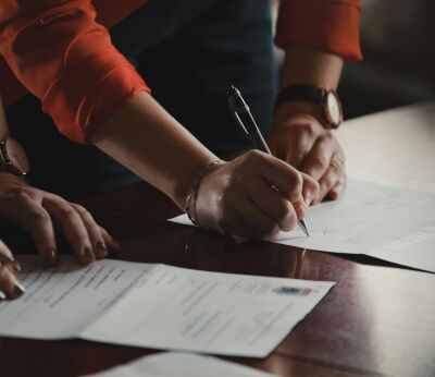 A woman in a long sleeve orange shirt signing mortgage documents