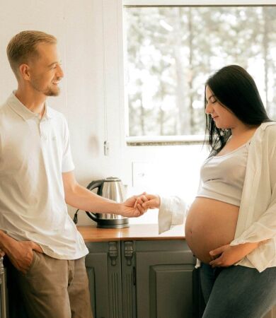 Pregnant woman standing in the kitchen holding her partners hand