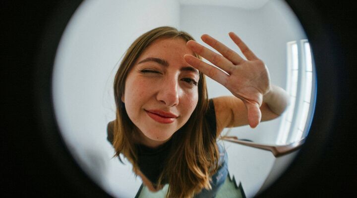 Woman holding up her hand and winking through a door's peephole