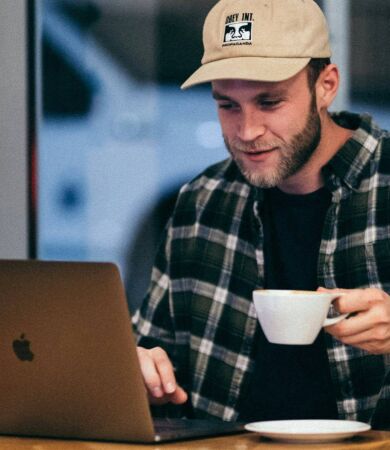 A man working on his laptop in a cafe while drinking a cup of coffee