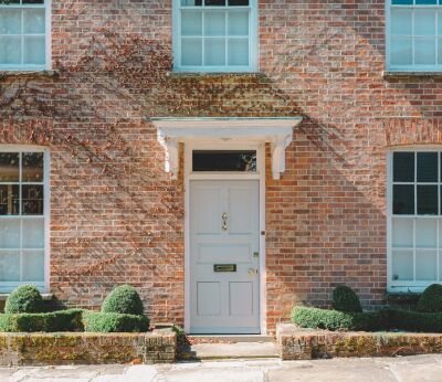 Brick house with ivy scaling the sides and a big grey door in the middle and green bushes outside the front
