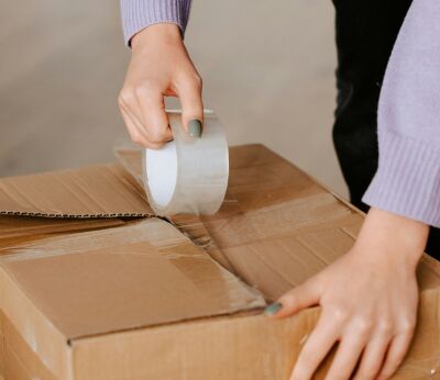 A woman in a purple jumper taping up a moving box on the floor