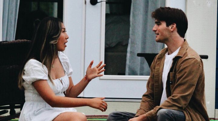 A couple talking to each other while sitting on the decking outside of their house