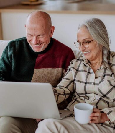A couple aged 50+ sitting on the sofa looking at their laptop