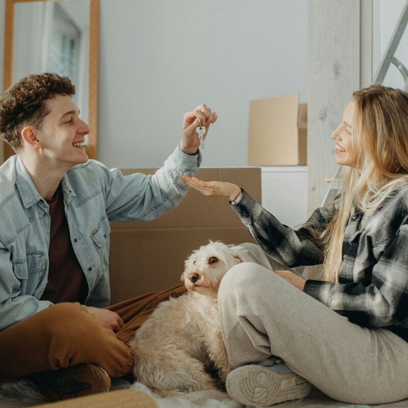 A man passing the keys to his partner in their new house with moving in boxes all around the room