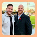 Two members of staff from The Levels Financial standing in front of the pitch during a Torquay United game