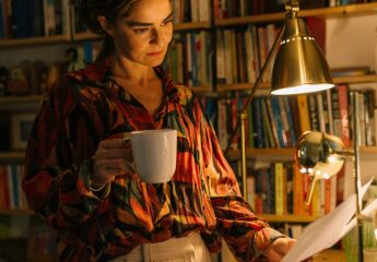 A woman in her library drinking a cup of tea and reading some documents