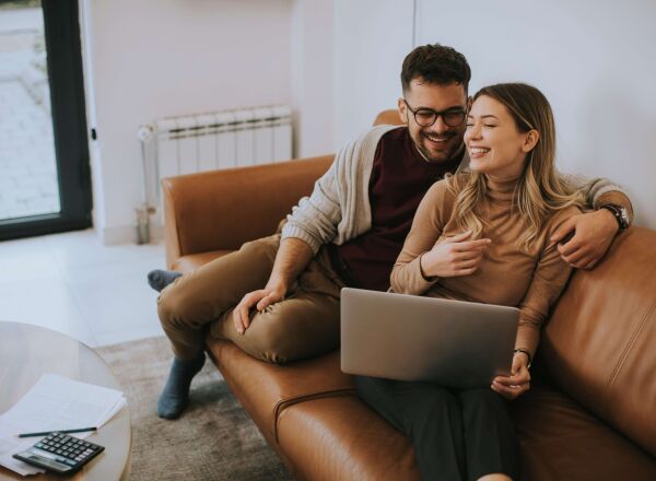A young couple laughing while on a call with a mortgage broker to secure their first-time buyer mortgage