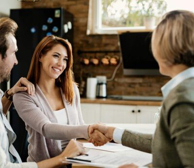 A woman shaking hands with a mortgage broker/advisor while her husband holds her shoulder