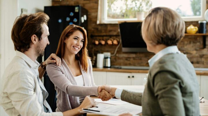 A woman shaking hands with a mortgage broker/advisor while her husband holds her shoulder