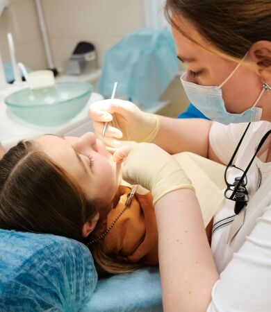 A female dentist using tools to examine the teeth of a young girl