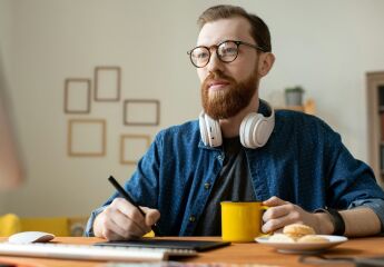 Young creative self-employed professional having a coffee while holding stylus over tablet
