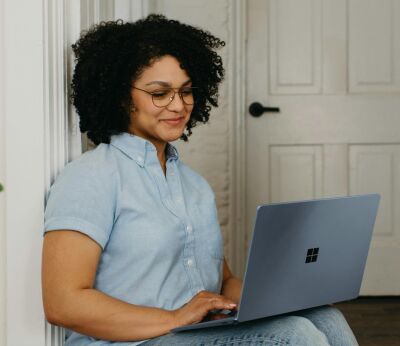 A woman sitting in a doorway while typing on her laptop