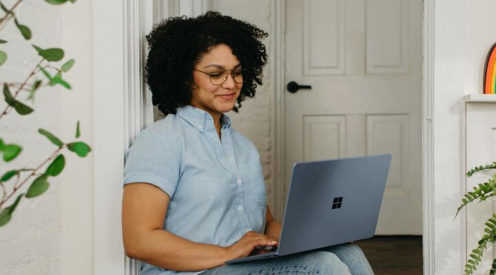 A woman sitting in a doorway while typing on her laptop