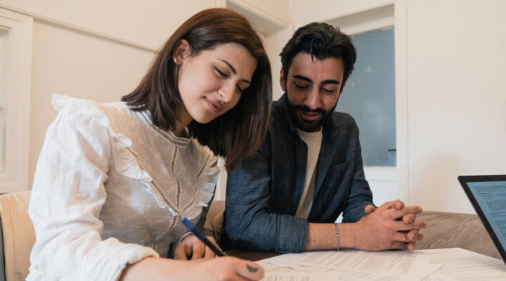A young couple sitting at a table signing a mortgage